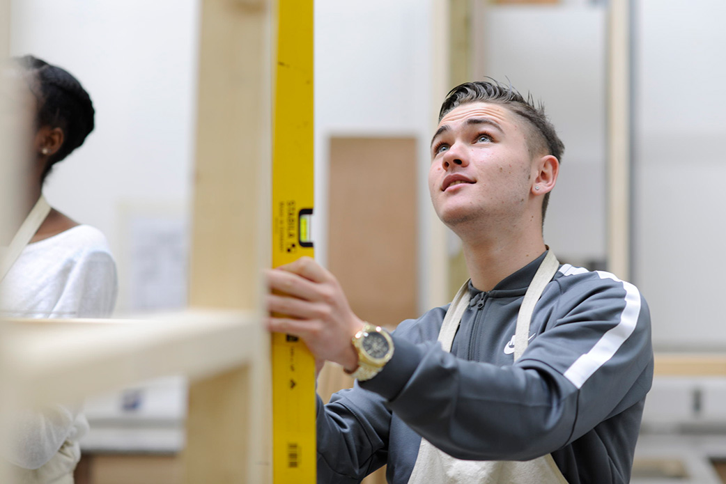A young man in a carpentry workshop uses a level to check for true vertical